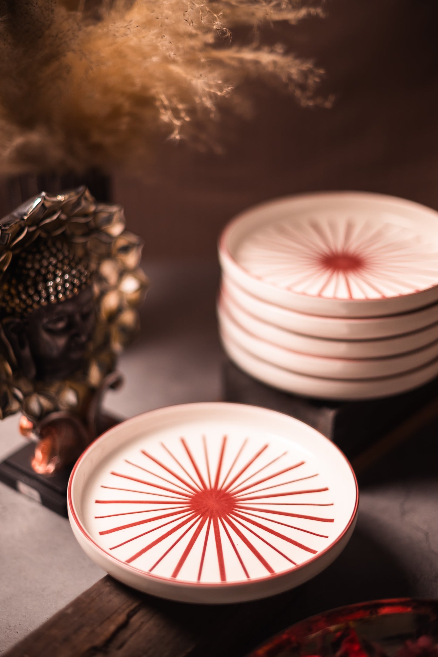 Stack of ceramic Round Snack plates with red sunburst design on a dark surface