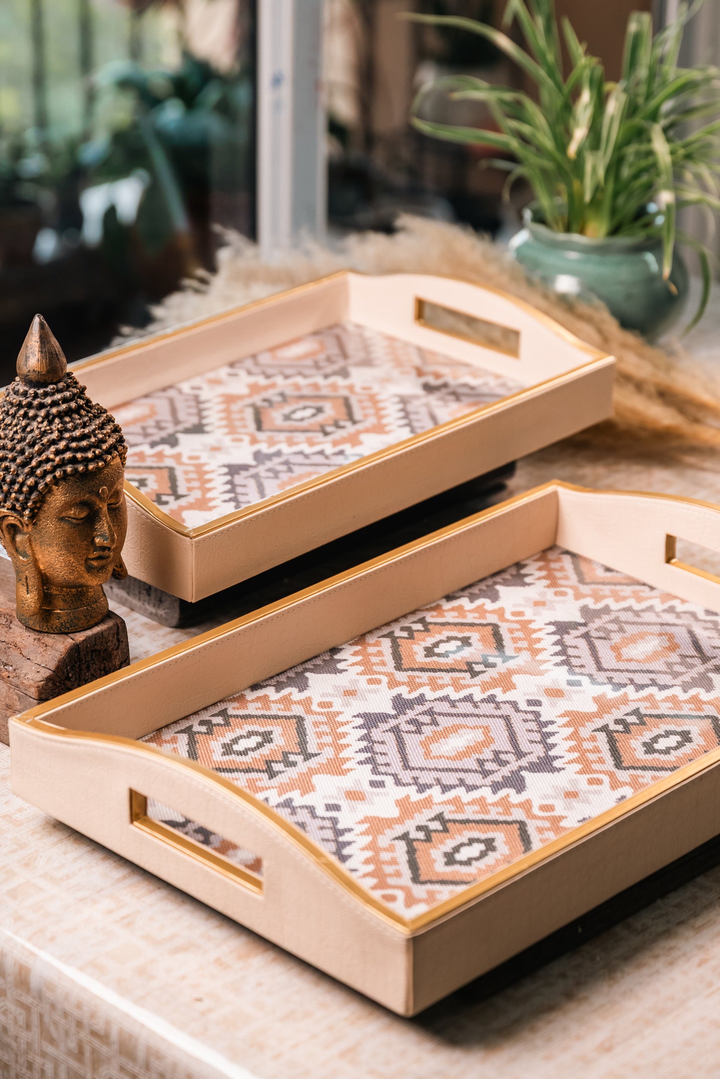 Leatherite trays with geometric patterns on a surface, with a Buddha statue and plants in the background.