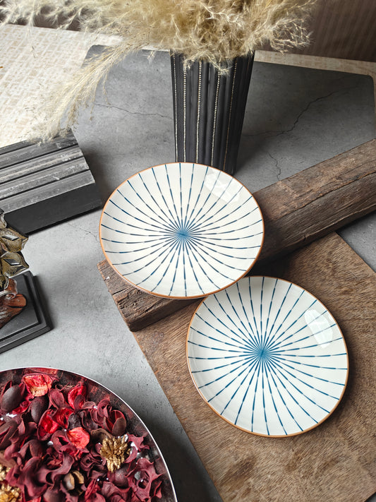 Two ceramic Sun Snack Plates with a sunburst pattern on a textured surface with dried flowers and wood.