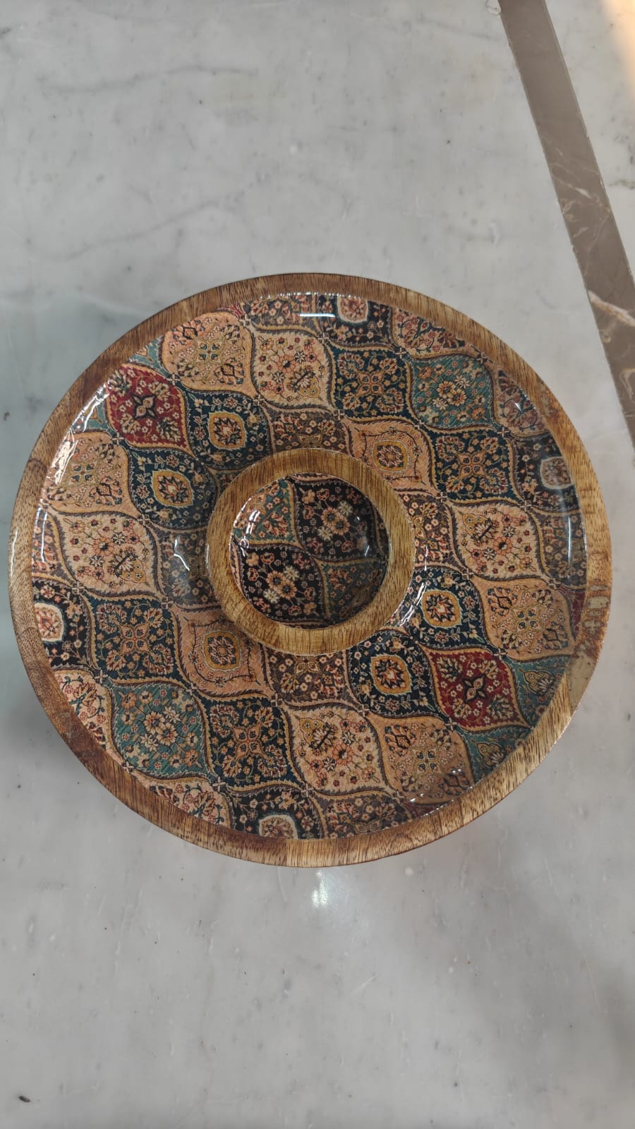 Decorative Wooden Round Chip-n-Dip Platter with Bowl with intricate patterns on a light-colored floor.
