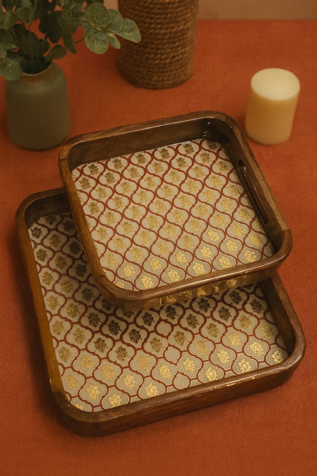 Two patterned trays on a red surface with a plant and candle in the background.